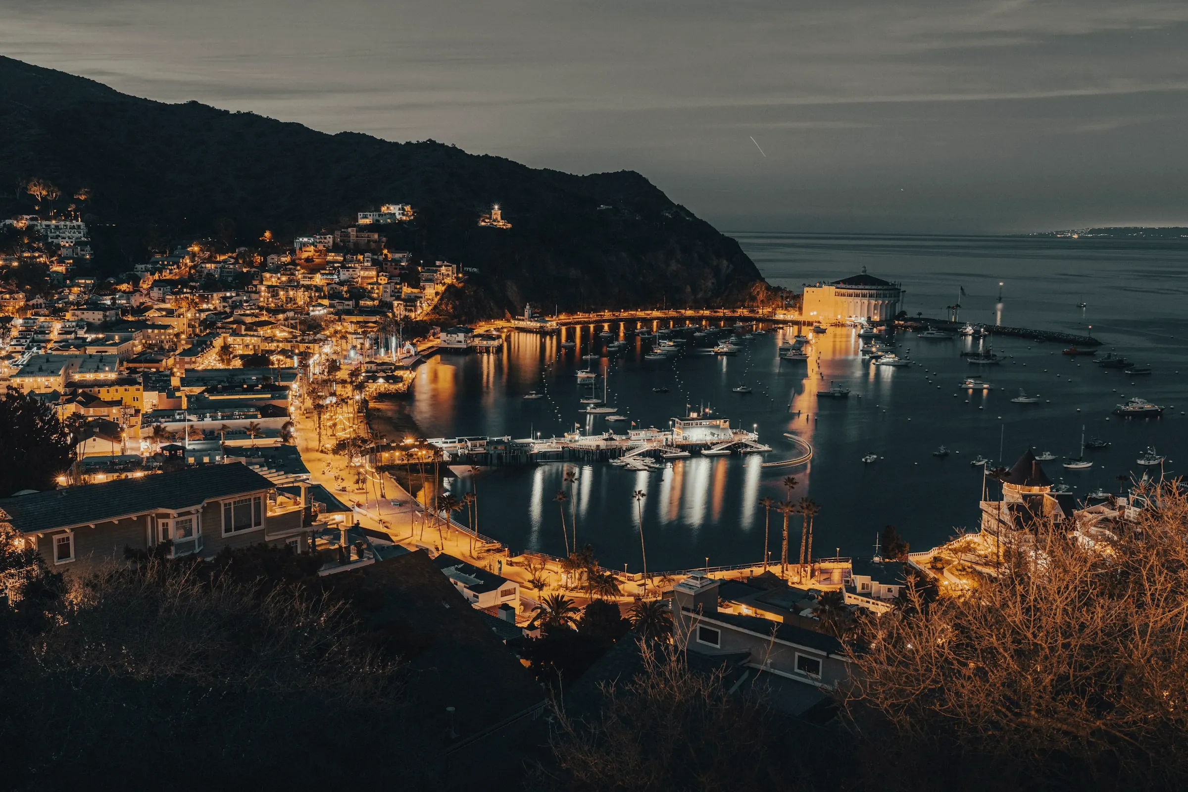 A hillside harbour town at blue hour, its lights reflected in the bay