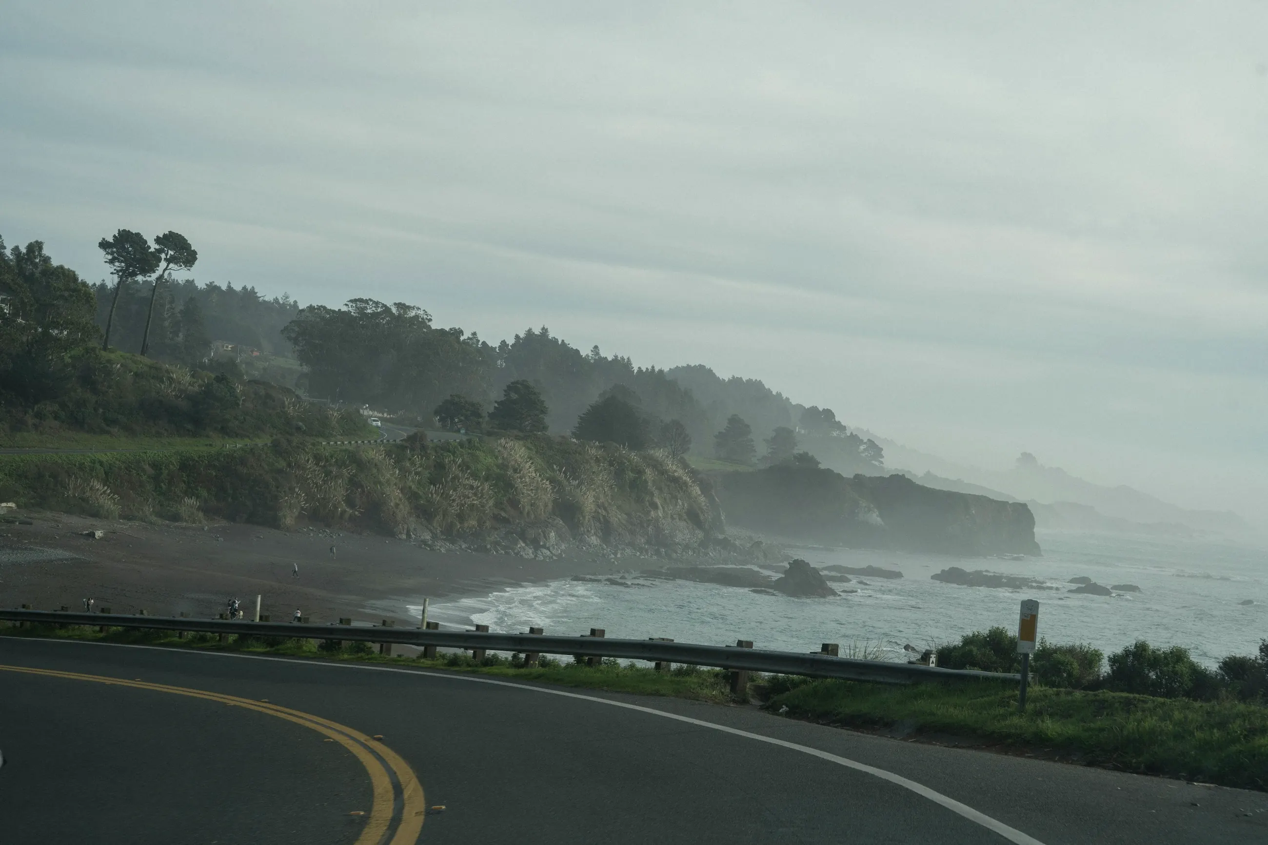 A coastal road curving past a misty headland and the sea