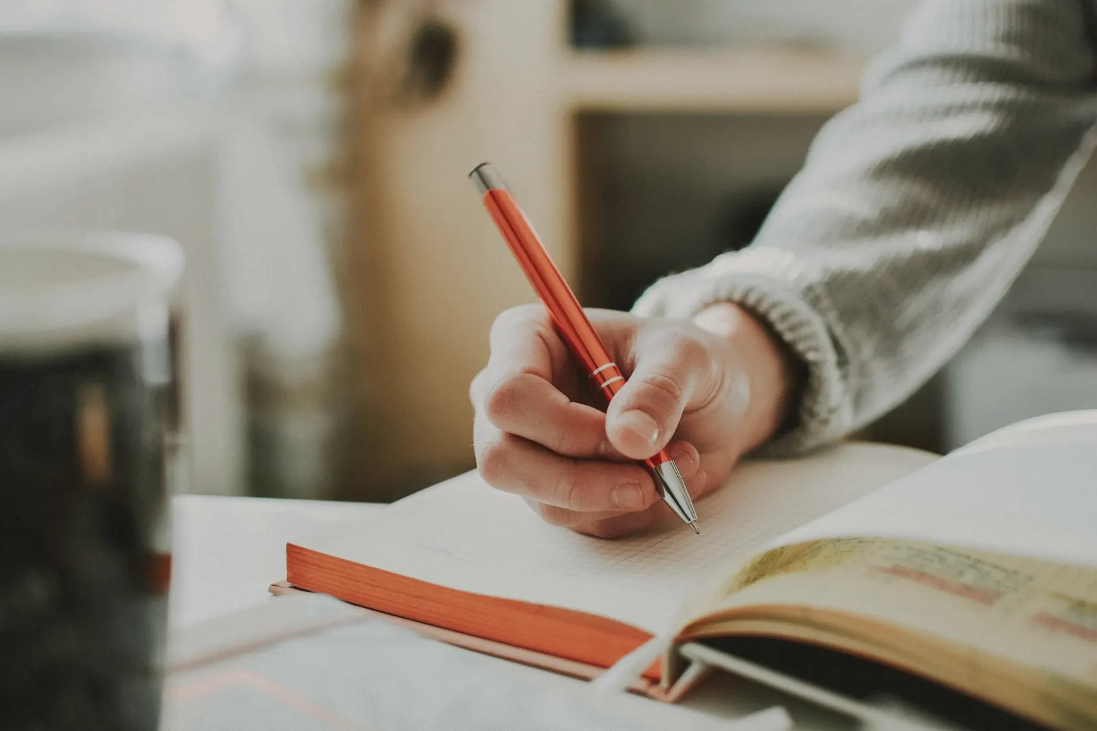A hand writing in a notebook with a red pen