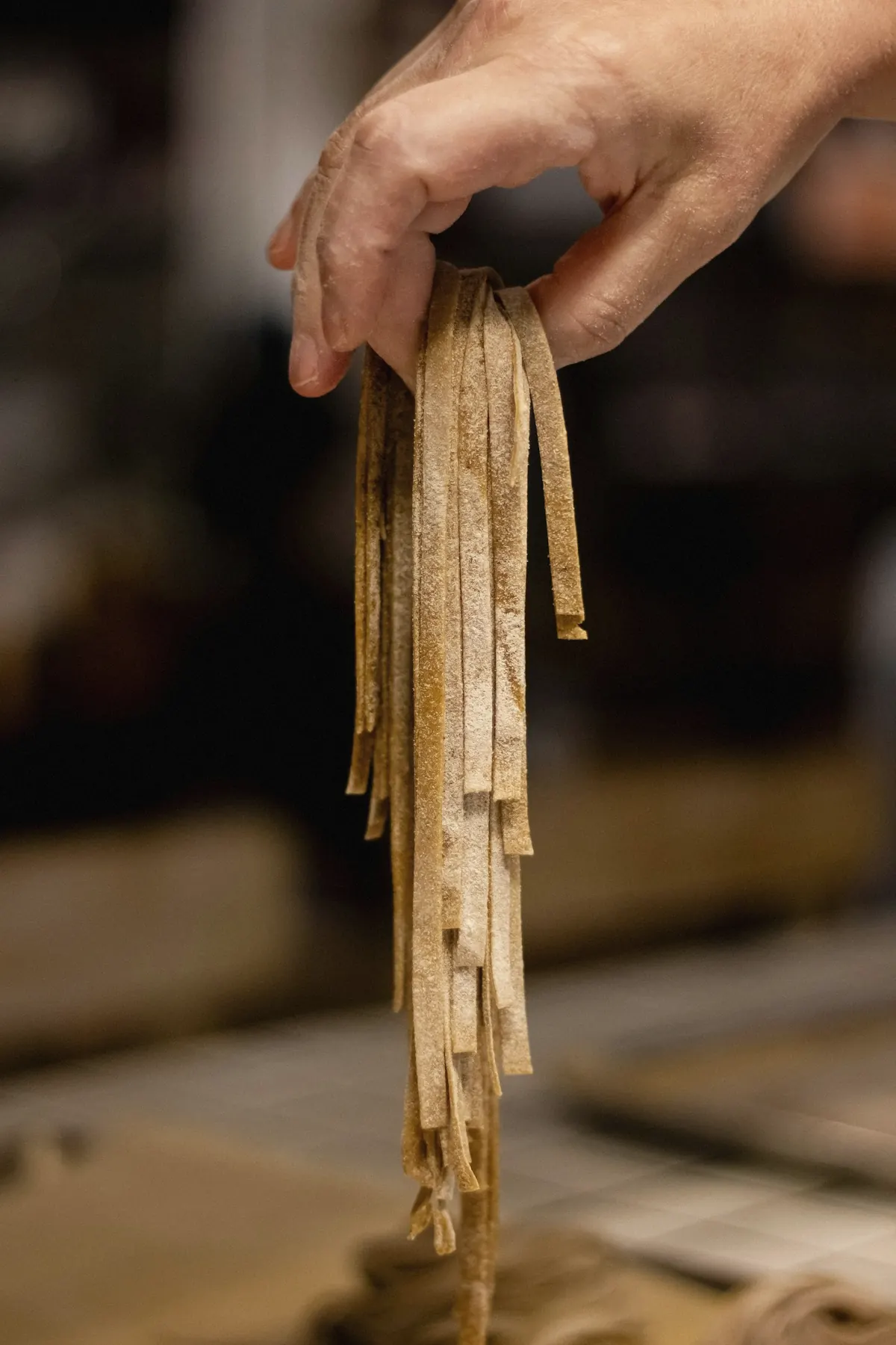 A hand lifting freshly cut ribbons of pasta in a warm kitchen